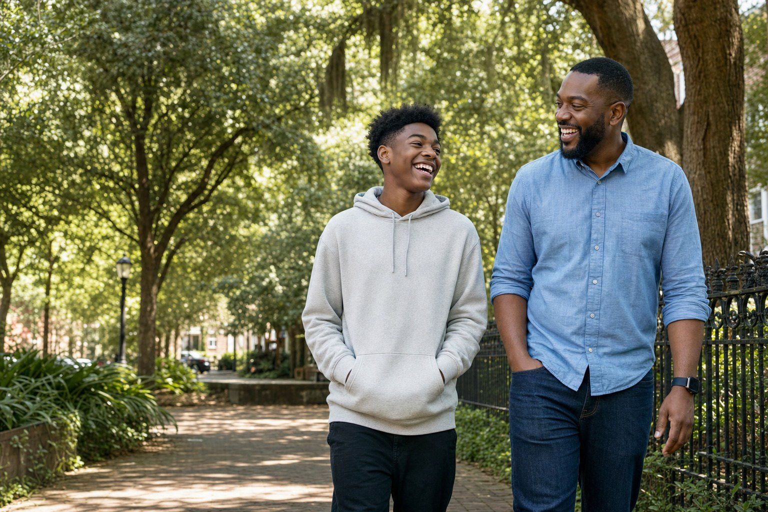 A teenage boy and adult mentor walking together beneath Savannah trees